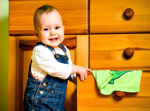 Young boy putting shirt in dresser drawer.