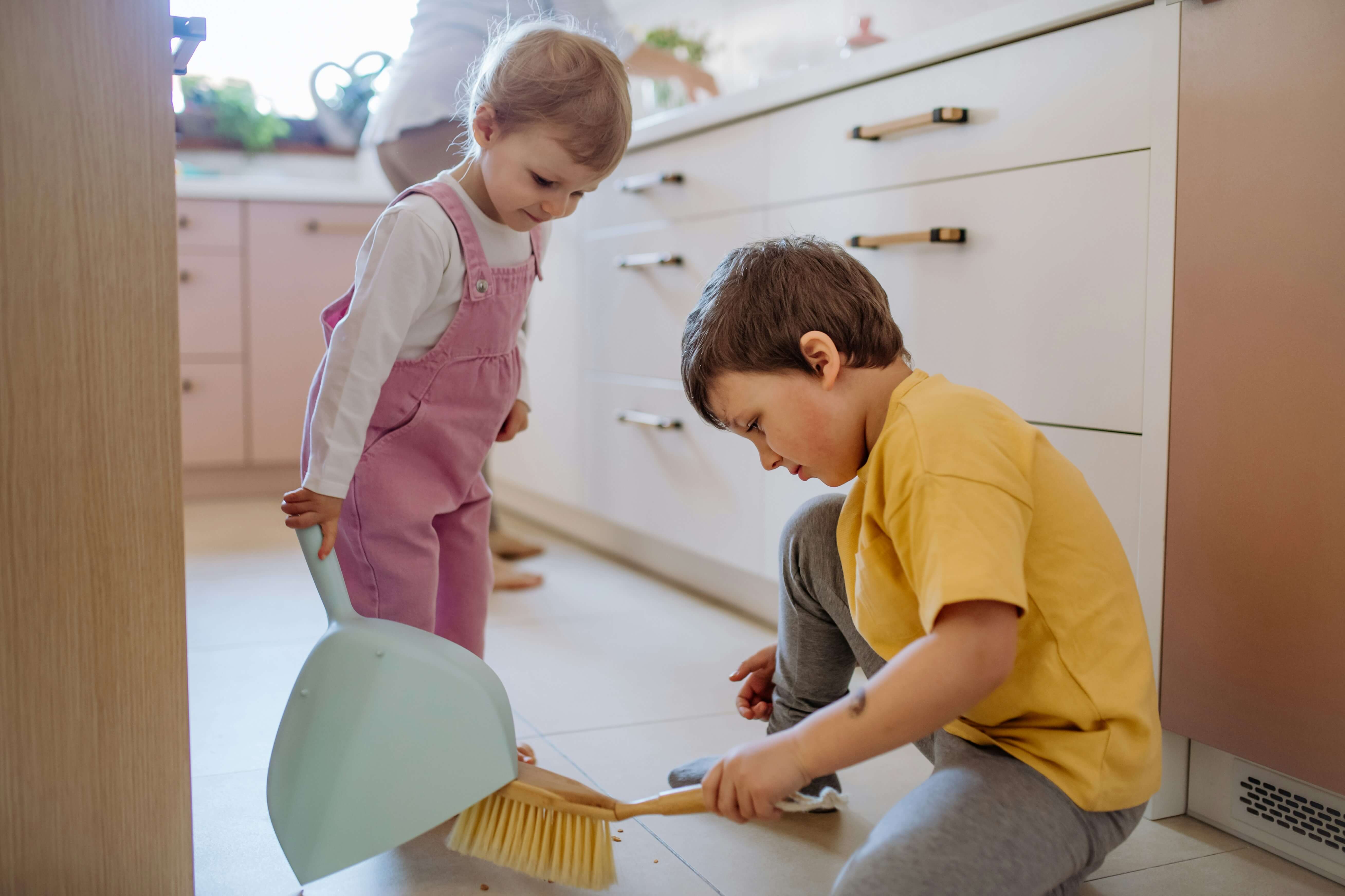 Two young boys are cleaning a kitchen floor.