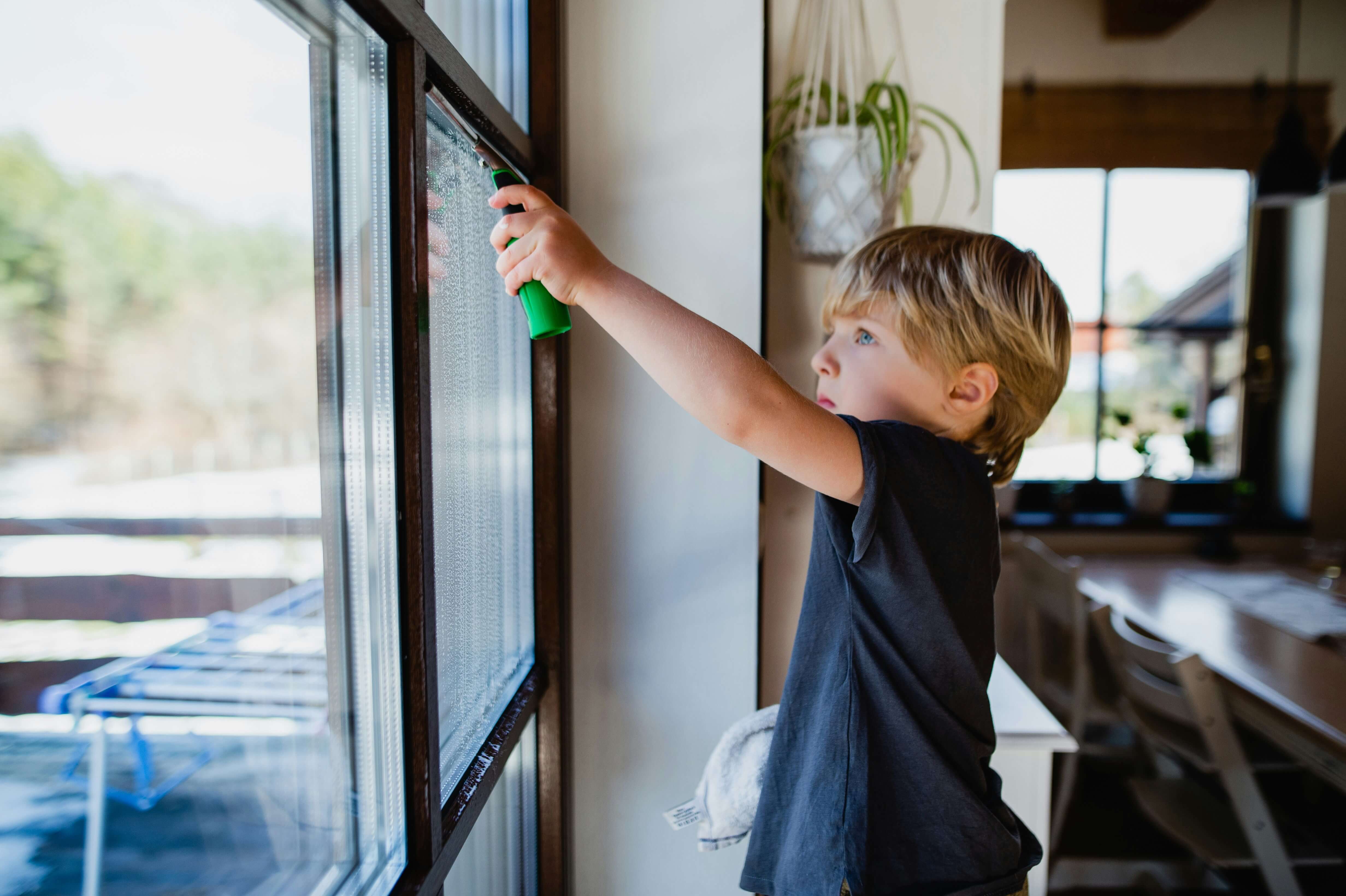 A young boy is cleaning a home window.