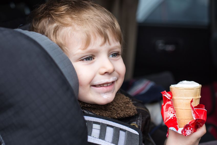 Young boy eating ice cream cone inside car.