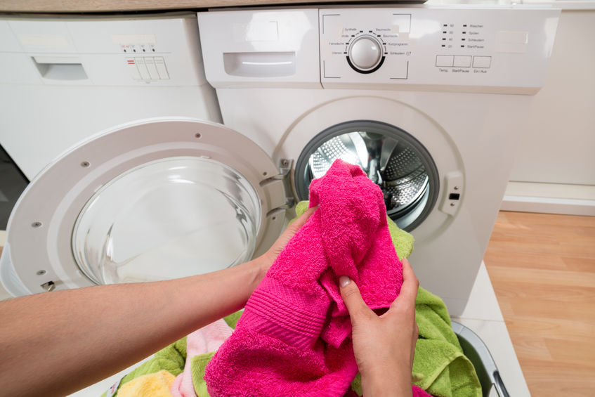 Woman putting pink towel into dryer.