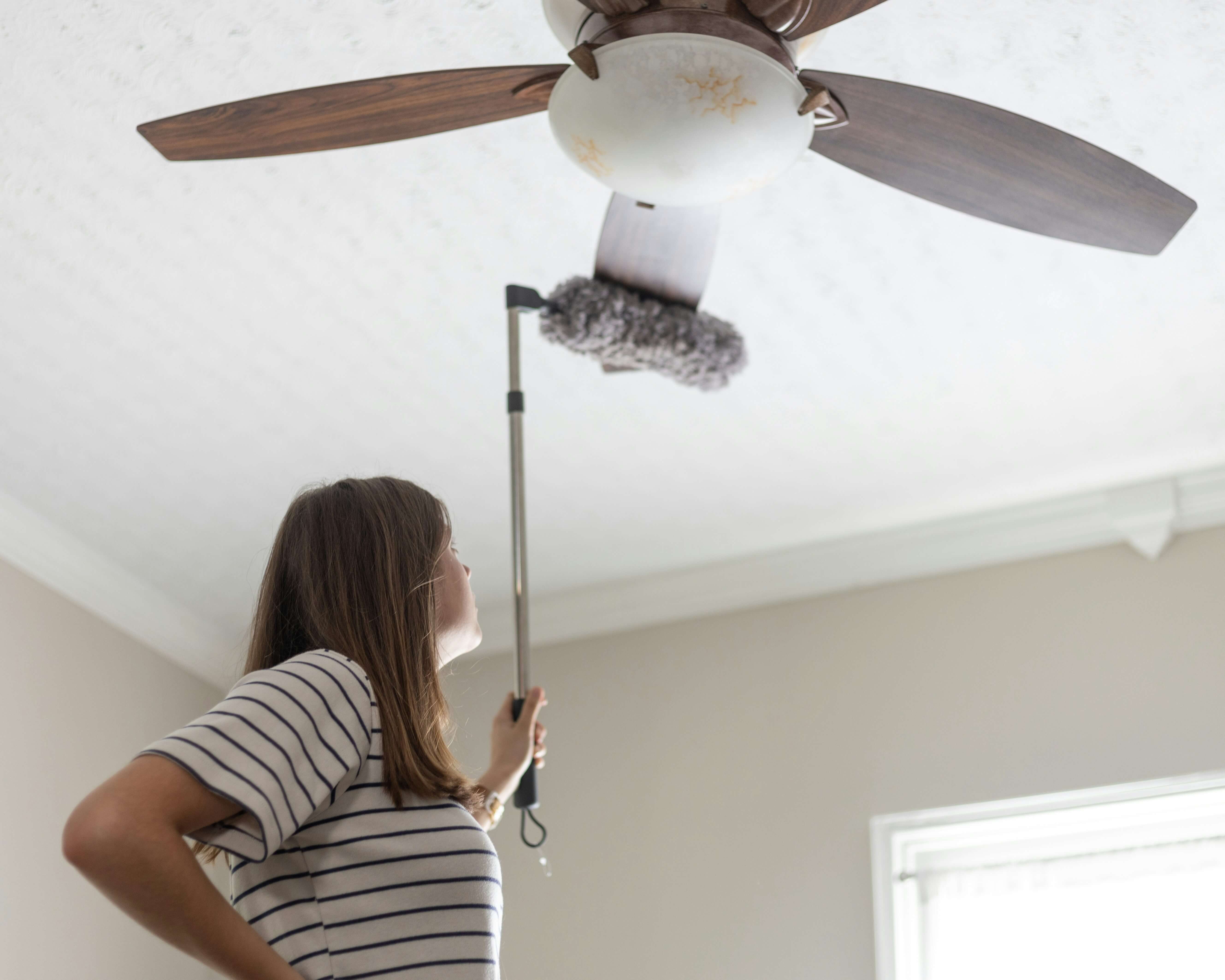 A woman cleaning a home's ceiling fan.