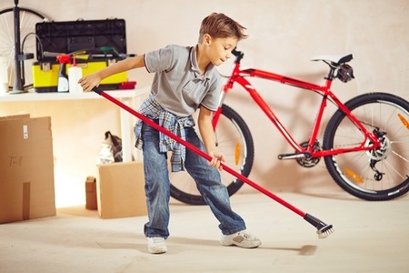 Young boy sweating garage floor with push broom.