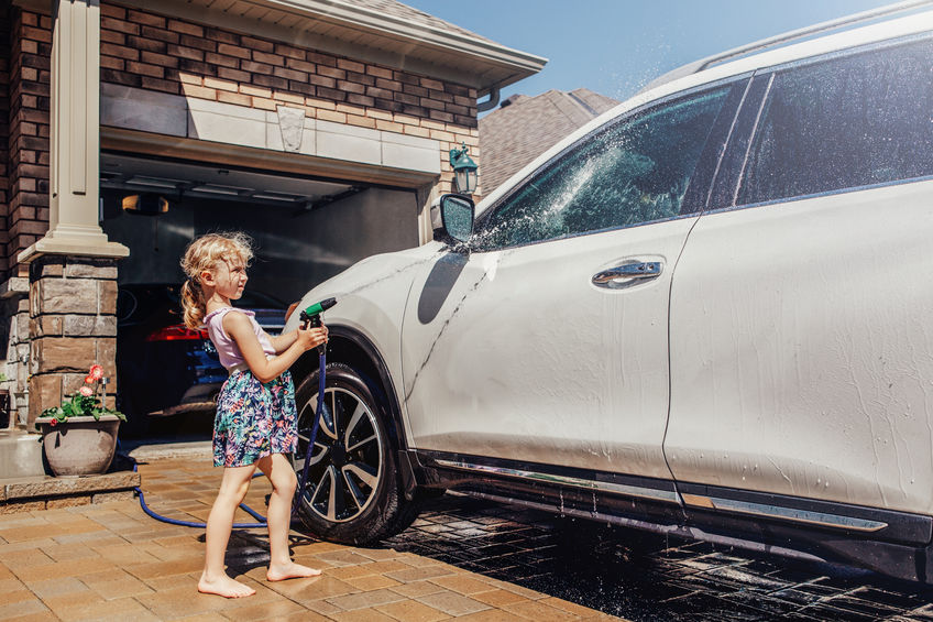 Young girl spraying car with garden hose,