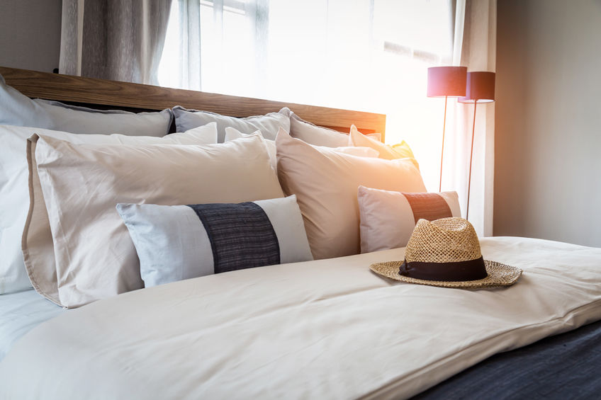 A bed with an assortment of decorative pillows and a traveler's hat on surface.