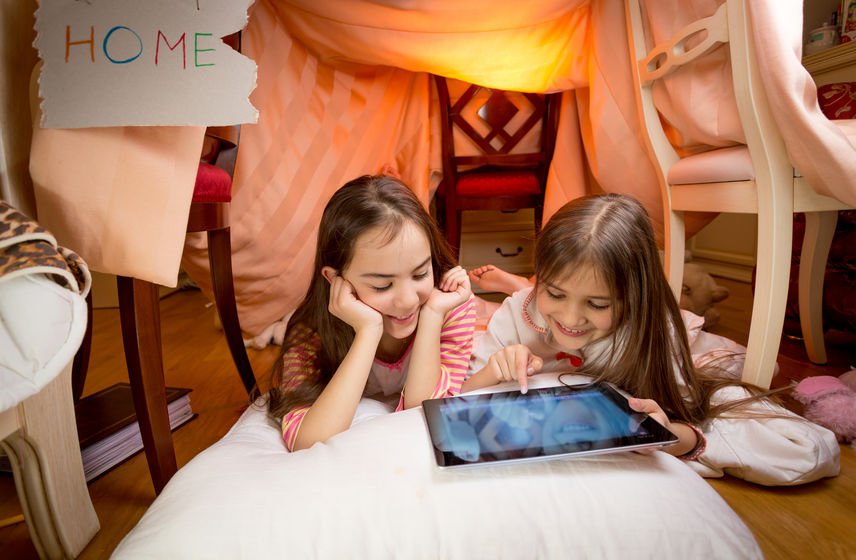 Young girls playing on computer inside bedroom fort.