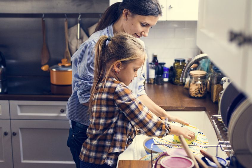 Mother washing dishes at sink with young girl.