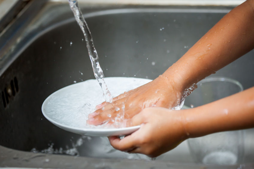 Child's hands washing plate in kitchen sink.