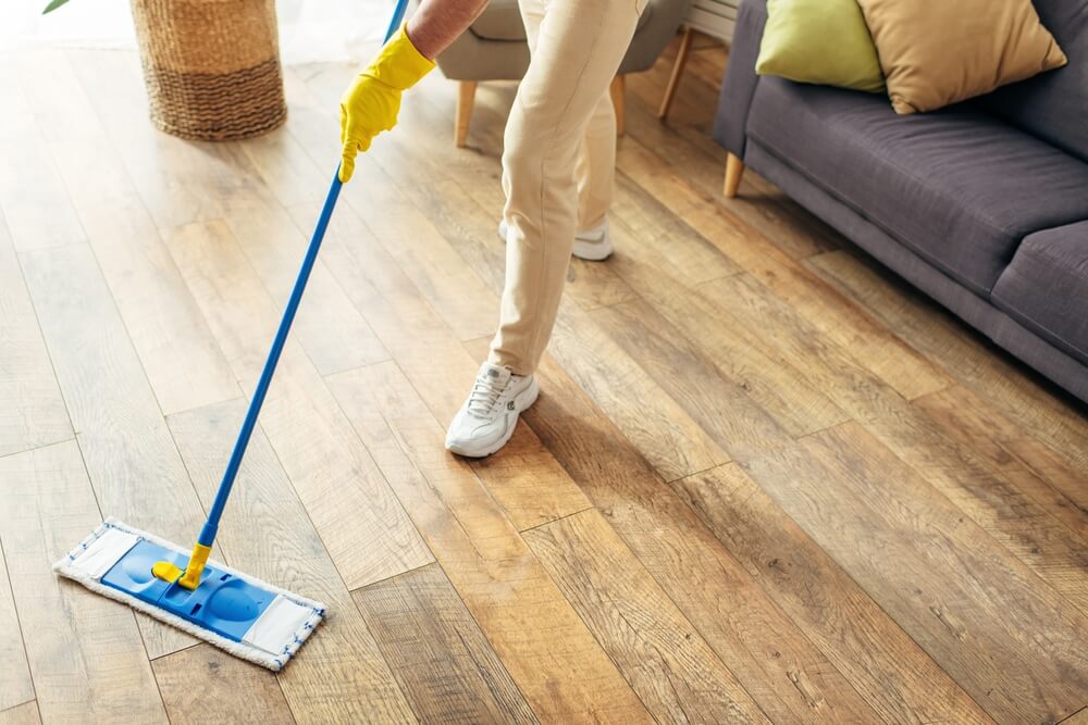 Legs of a man cleaning a wooden floor.
