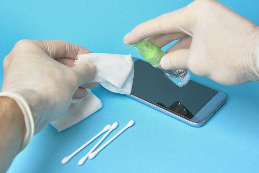 Gloved hand cleaning phone with alcohol spray.