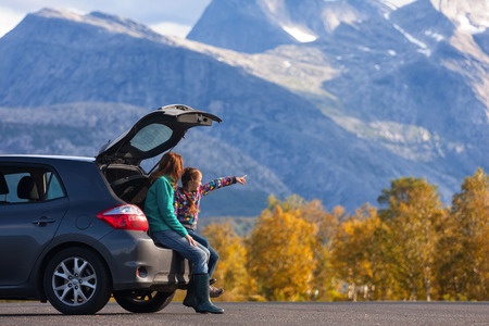 Parent in child sitting in minivan hatchback looking at mountains.