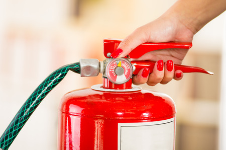 Woman's hand on fire extinguisher handle.