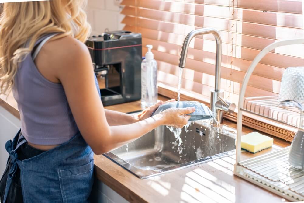 Woman hand-washing dishes in the kitchen sink.